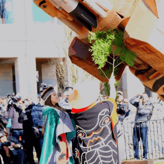 People in ceremonial clothing blessing a totem pole