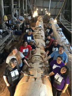 People in carving studio helping to carve a totem pole