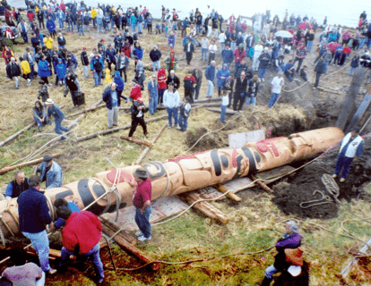 Crowd watches while a totem pole is raised