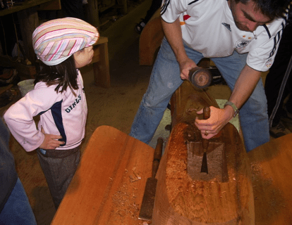 Young girl watches as man carves totem pole