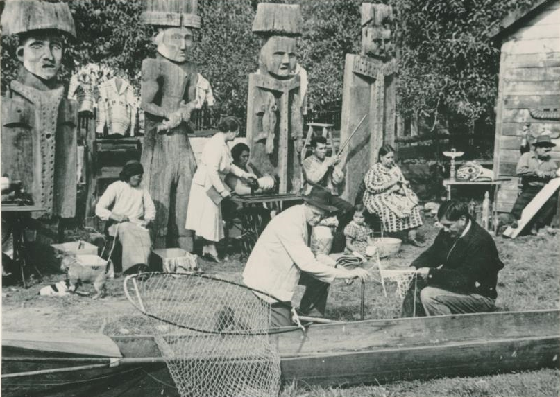 A group of people crafting in front of four house posts.