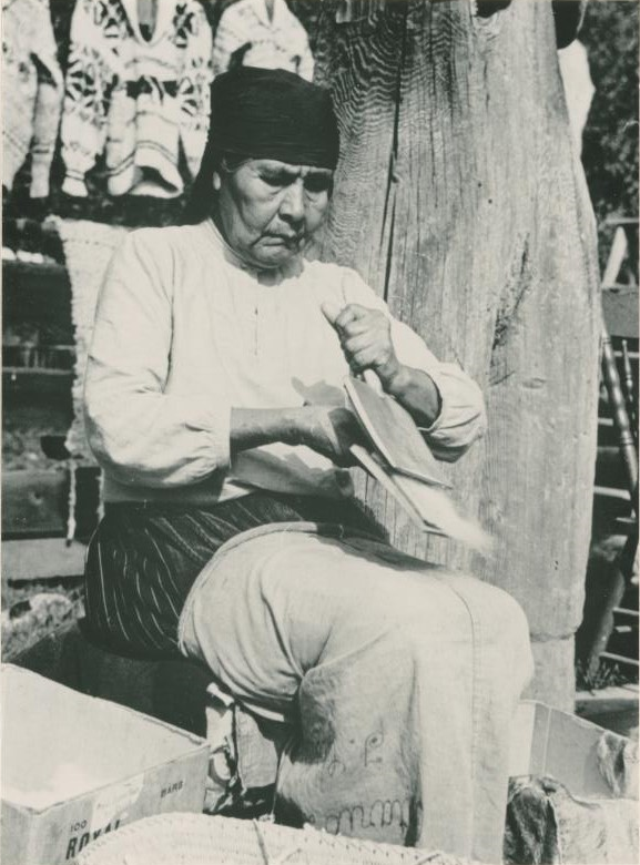 Vieille dame assise devant un poteau de maison travaillant avec la laine. 