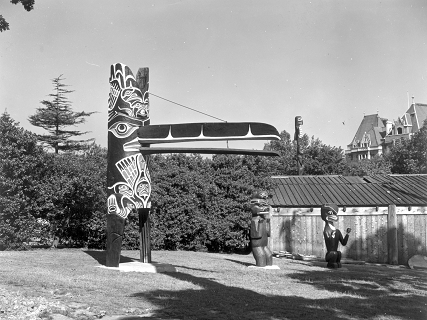 House entrance pole shown in Thunderbird Park beside carved figures of bears. 