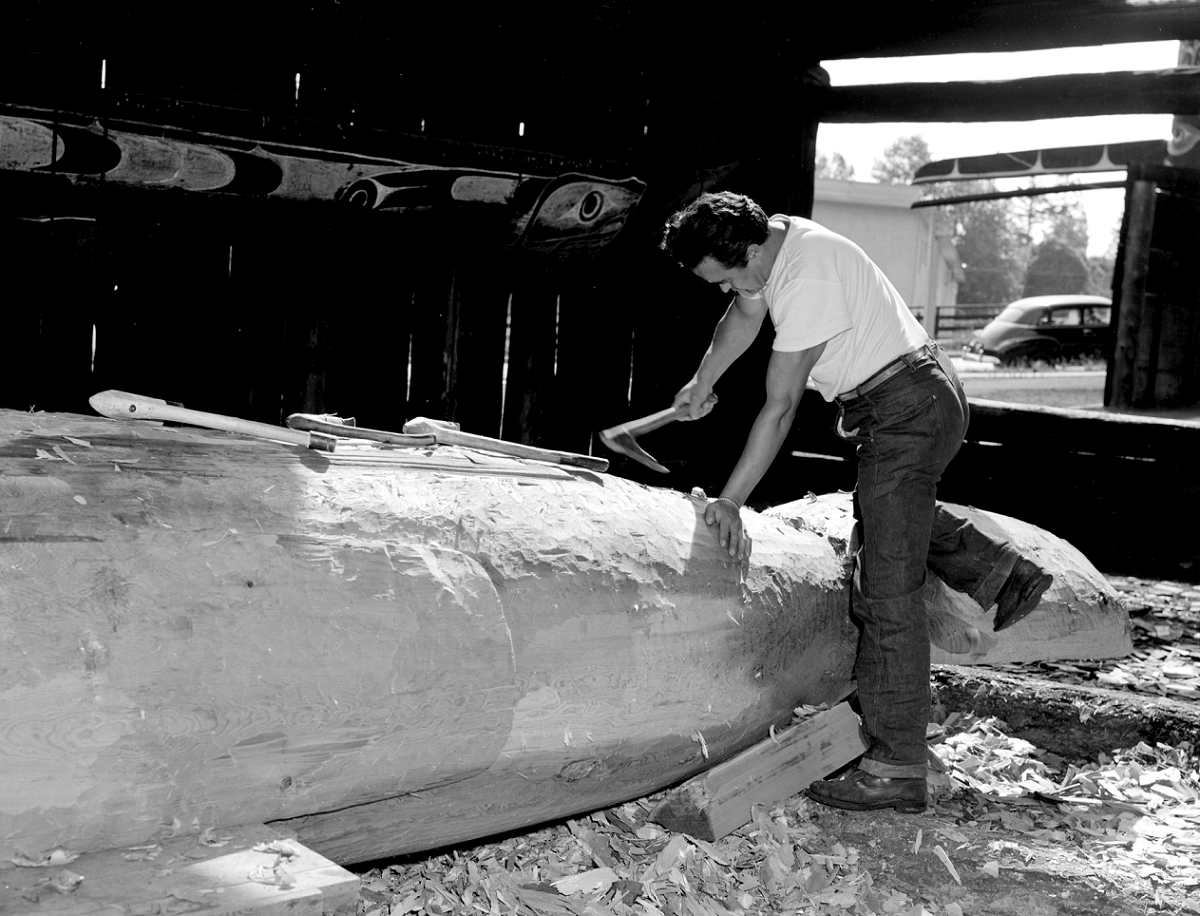 Man carving a large log with a tool.