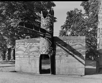 Poteau d'entrée de maison dans le parc Thunderbird entre des écrans cérémoniels en bois peint.