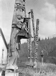 Side view of five poles and a carved figure standing in a line.