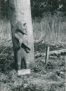 Carved figure of a man holding an axe with the axe blade missing. 