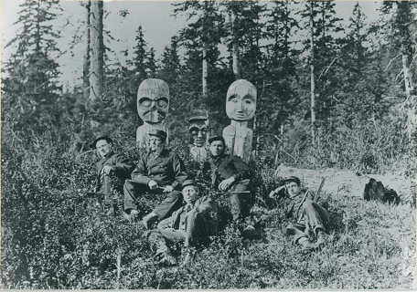 Men in uniforms sitting and laying in front of two carved grave posts.