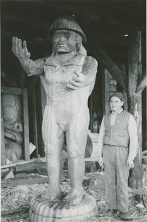 Man standing beside tall carved welcome figure.