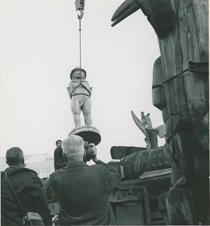 Carved welcome figure being lifted by crane onto a truck bed.