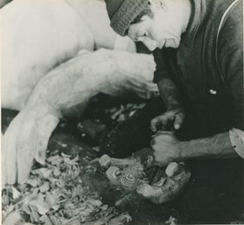 Man leaning over and working on the hand of the carved figure.