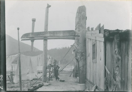 Side view of house entrance pole with long raven’s beak extending over boardwalk. 