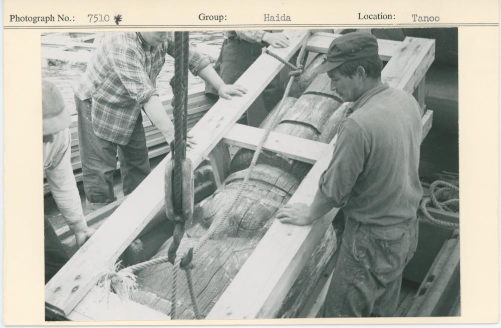 Men with a crated piece of the house frontal pole loading it onto a boat.