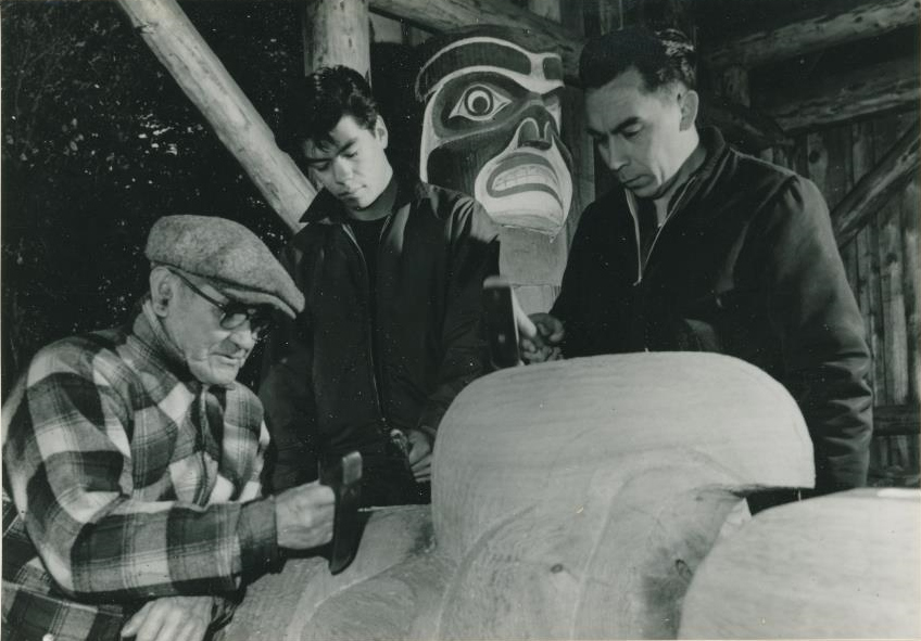 Trois hommes regardant et travaillant sur un poteau.