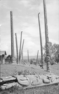 Old totem pole lying on its side in front of a group of totem poles