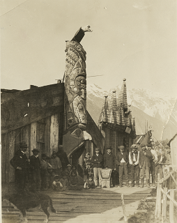 People standing in front of totem pole with entrance in totem's mouth