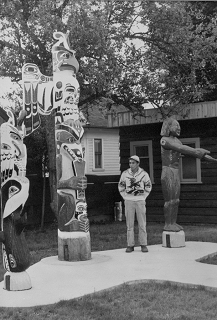 Man stands among a group of totem poles