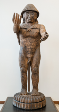 Carved wooden human figure with arms outstretched in a welcome.