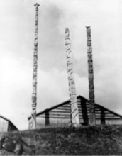Three totem poles stand in front of a house